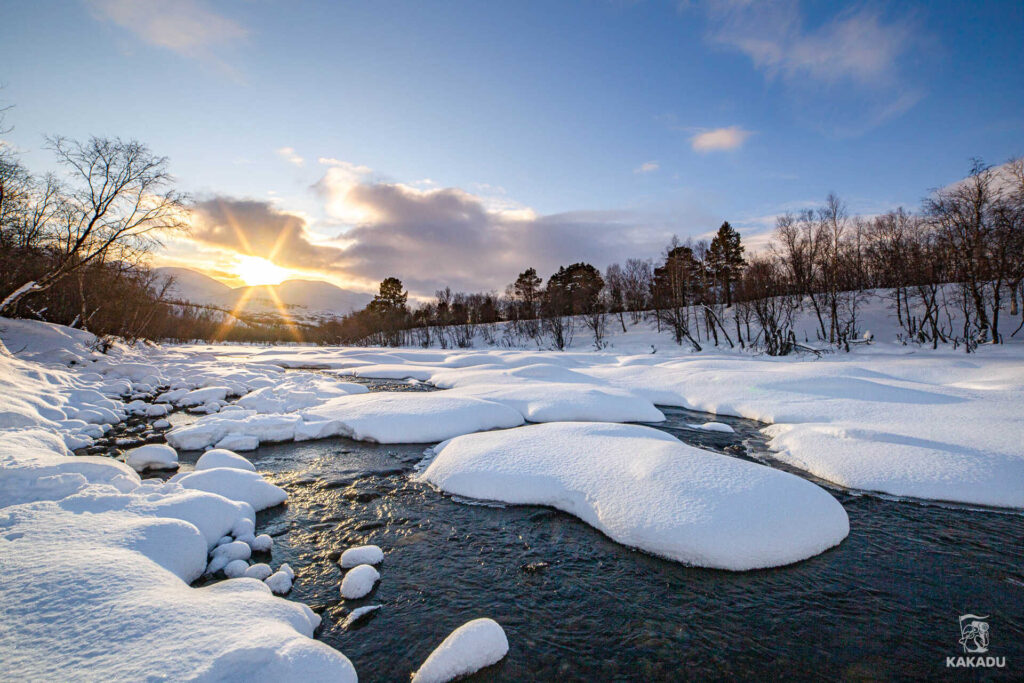 Niskie, polarne słońce nad zmrożoną rzeką Abiskojokk, w Parku Narodowym Abisko